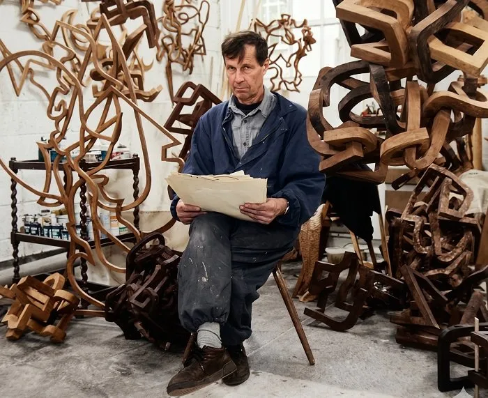 Oleg Prokofiev seated among his wooden sculptures